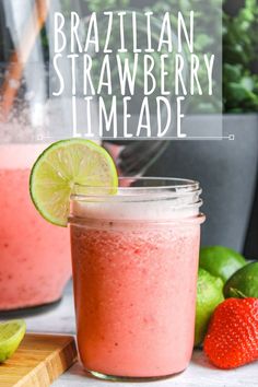 a strawberry limeade smoothie in a mason jar next to fresh strawberries and limes