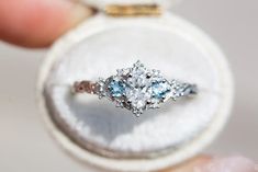 an engagement ring with three blue and white stones in it's center is being held by someone