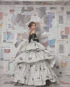 a woman in a dress made out of newspapers is standing against a wall covered with newspaper clippings