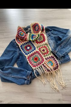 a crocheted scarf laying on top of a pair of denim pants and jean jacket