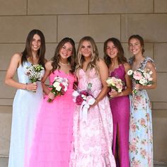 a group of young women standing next to each other in long dresses and holding bouquets