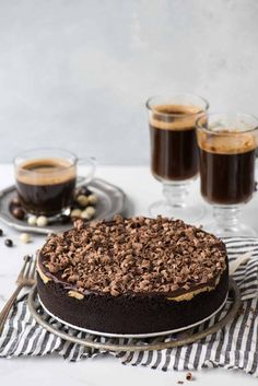 a chocolate cake sitting on top of a table next to two cups of coffee and spoons