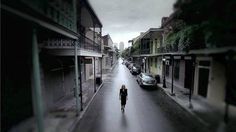 a woman walking down the middle of a street with cars parked on both sides of it