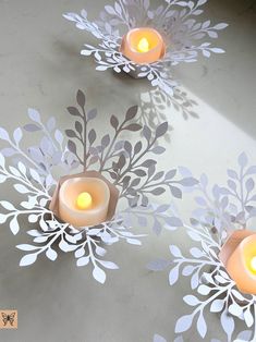 three lit candles sitting on top of a table next to paper cut flowers and leaves