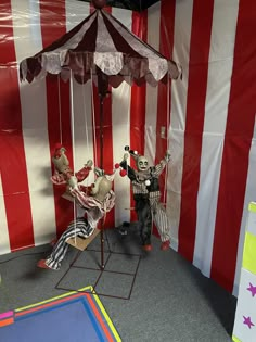 two creepy clowns sit under an umbrella in front of a circus tent with red and white striped walls