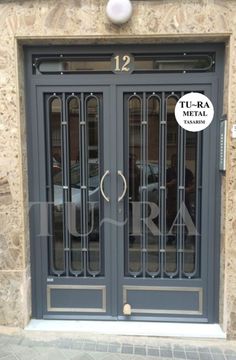 the entrance to a building with two glass doors and numbers on each door, in front of a stone wall