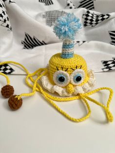 a crocheted yellow hat with googly eyes and a blue pom - pom