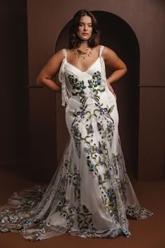 a woman in a white dress with flowers on the side and her hands on her hips