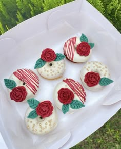 four decorated cookies sitting on top of a white tray next to green plants and grass