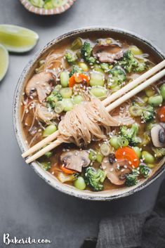 a bowl filled with noodles, broccoli and carrots next to lime slices