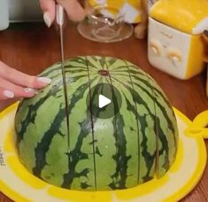 someone cutting into a large watermelon on top of a wooden table with scissors