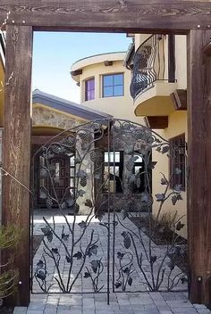 an iron gate with flowers on it in front of a large house and stone walkway