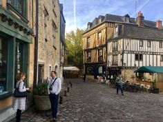 two people standing on the side of a cobblestone street in an old european town