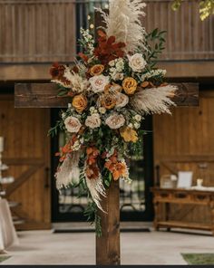 a cross decorated with flowers and feathers in front of a wooden building at a wedding