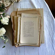 three open books sitting on top of a table next to white flowers and an old book