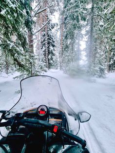 a snow covered motorcycle driving on a snowy road in the woods with lots of trees