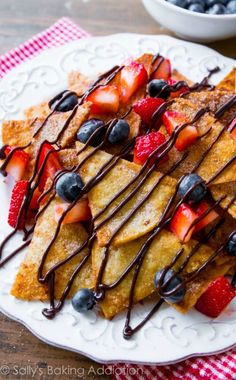 a white plate topped with french toast covered in chocolate and strawberries next to a bowl of blueberries