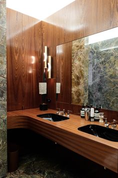 a bathroom with two sinks and mirrors in front of wood paneled walls, along with marble flooring