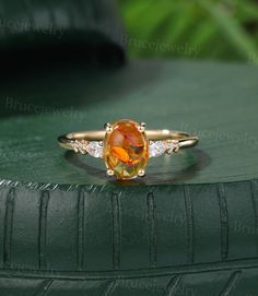 an orange and white diamond ring sitting on top of a green leather cushioned surface