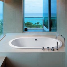 a large white bath tub sitting in a bathroom next to a tall window with an ocean view