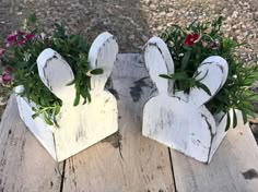 two white wooden bunny shaped planters with flowers in them sitting on a wood table