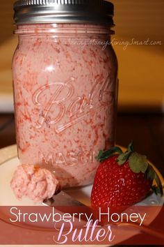 a strawberry and honey butter in a mason jar with a spoon next to it on a plate