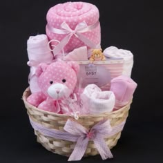 a pink teddy bear sitting in a basket filled with blankets and other baby items on a black background