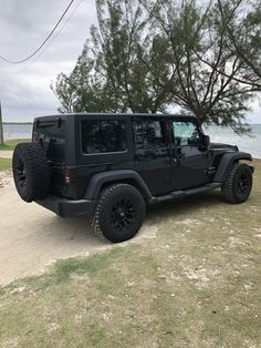 a black jeep parked on the side of a dirt road next to a body of water