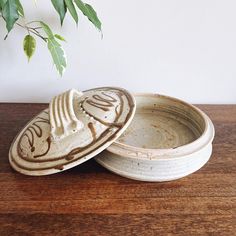 two white bowls sitting on top of a wooden table next to a plant in a vase