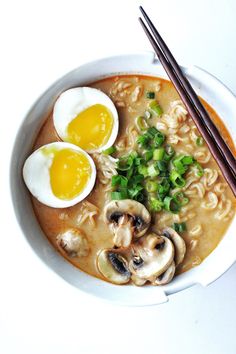 a bowl filled with noodles, mushrooms and eggs next to chopsticks on a white surface