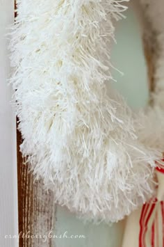 a white stuffed animal hanging from the side of a wooden door with a red and white striped ribbon