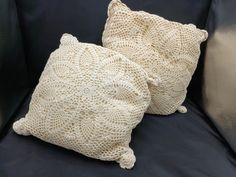 two crocheted pillows sitting on top of a black couch next to each other