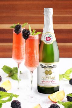 two wine glasses filled with champagne and blackberries next to a bottle of sparkling wine