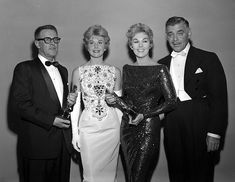 an old black and white photo of three men and two women in formal wear standing next to each other