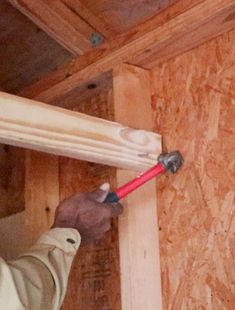 a man holding a hammer in his hand while working on a wall with plywood