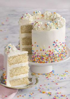 a white cake with sprinkles and a slice missing from it on a plate