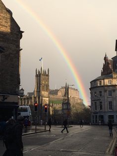 a rainbow is seen in the sky over an old city street with people walking on it