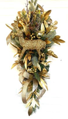 a christmas wreath hanging on the side of a white wall with gold and green decorations