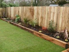 a wooden fence is next to a grassy area with flowers and plants in the middle