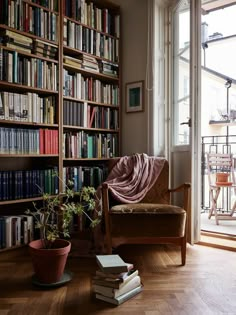 a living room filled with lots of books on top of a hard wood floor next to a window