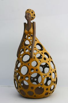 a ceramic figurine sitting on top of a yellow vase with holes in it