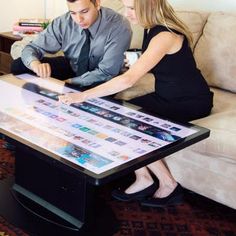 a man and woman are sitting at a table looking at pictures on the glass top