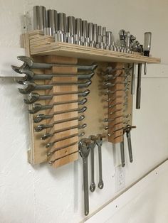 there are many wrenches hanging on the wall and in front of it is a shelf with tools