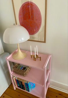 a pink shelf with some books on it and a lamp in the corner next to it