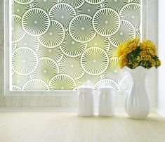 a white vase with yellow flowers in front of a glass window that has circular designs on it