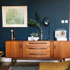 a living room with blue walls and wooden furniture, including a sideboard that has plants on it