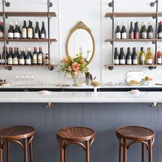 three stools in front of a bar with wine bottles on the wall behind it