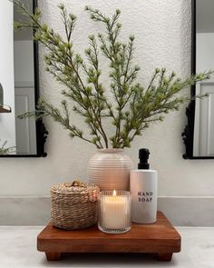 a candle and some plants on a table in front of a mirror with two mirrors behind it