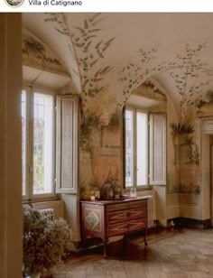 a room with many windows and paintings on the walls, along with a dresser in the center