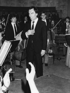 a man in a suit and tie standing next to an orchestra with music instruments behind him